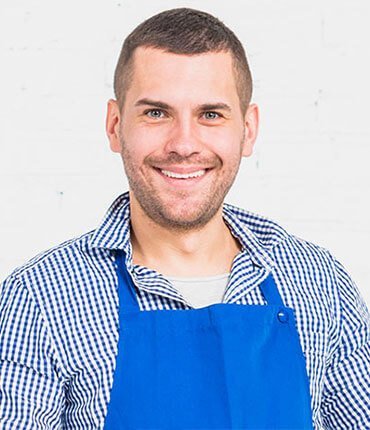 Smiling man in a blue apron, representing the team at Desert Mesa Painting, showcasing expertise in painting services.