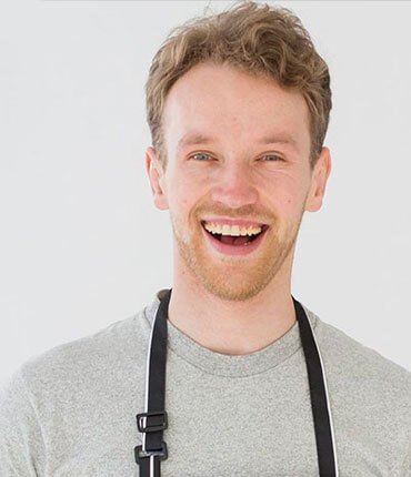 Smiling young man in a gray shirt with an apron, representing the team at Desert Mesa Painting, emphasizing customer-focused service and craftsmanship.